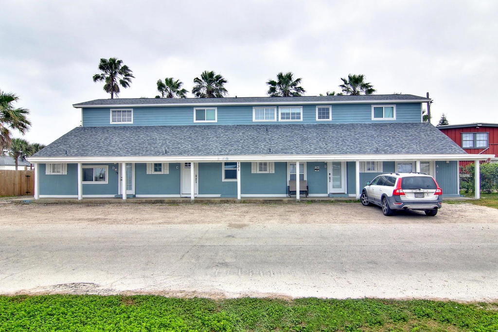 Charming blue duplex property with convenient parking and tropical palm trees creating a welcoming arrival experience.