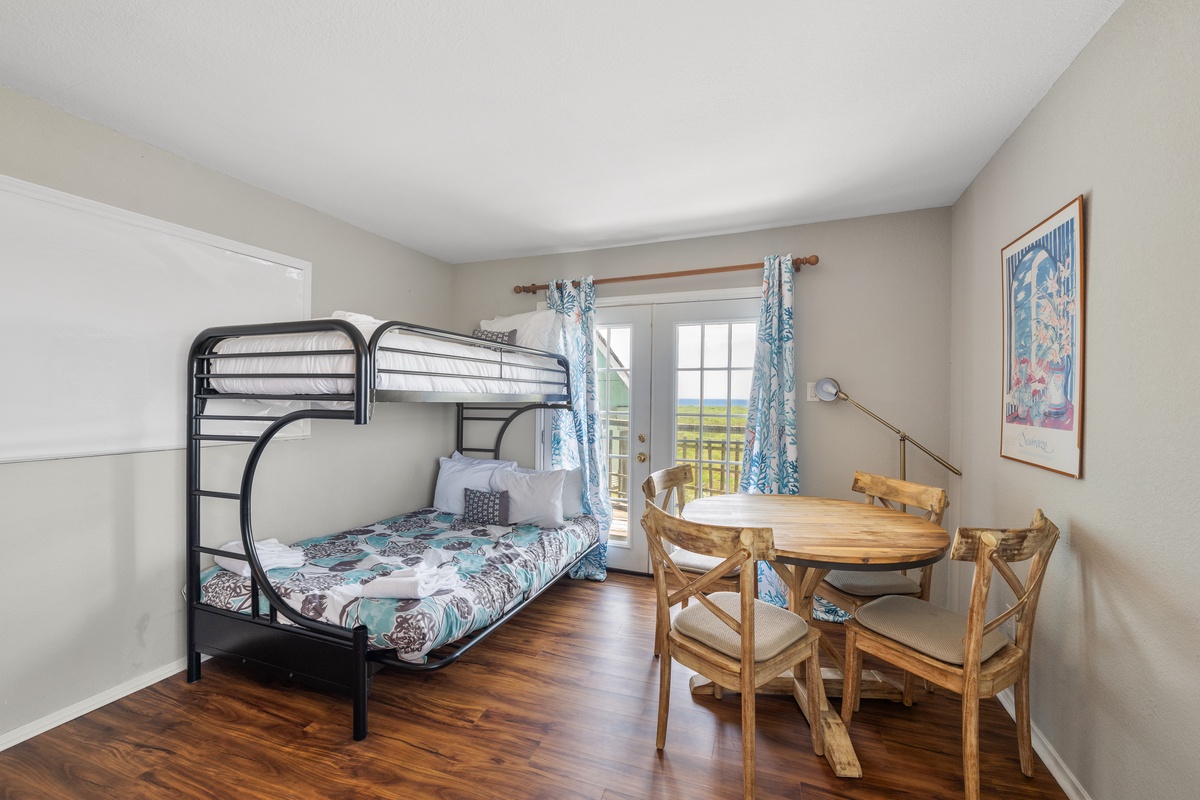 Your cozy sleeping space features a practical bunk bed and charming wooden dining area, with doors opening to a peaceful view of surrounding fields.