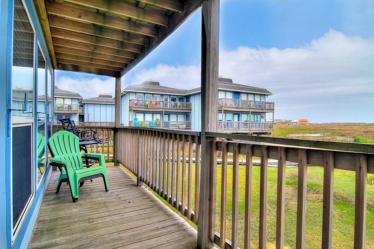 Relax on your private covered deck with coastal views and comfortable seating overlooking the peaceful grassy landscape.