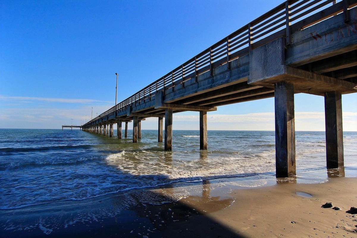 A wooden pier extends into the sparkling ocean waters, creating a scenic coastal landmark near your beachfront retreat.