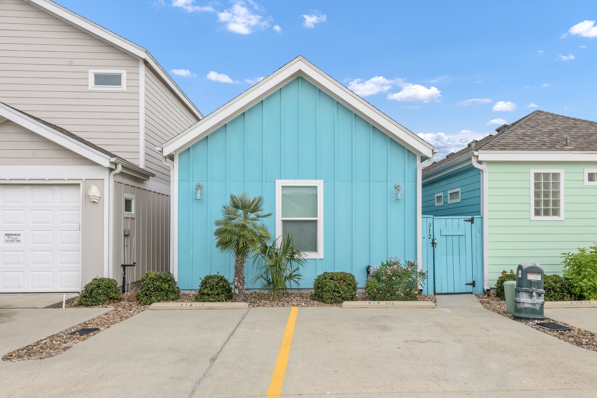 Charming turquoise cottage with tropical landscaping and dedicated parking space in a colorful beachside community.