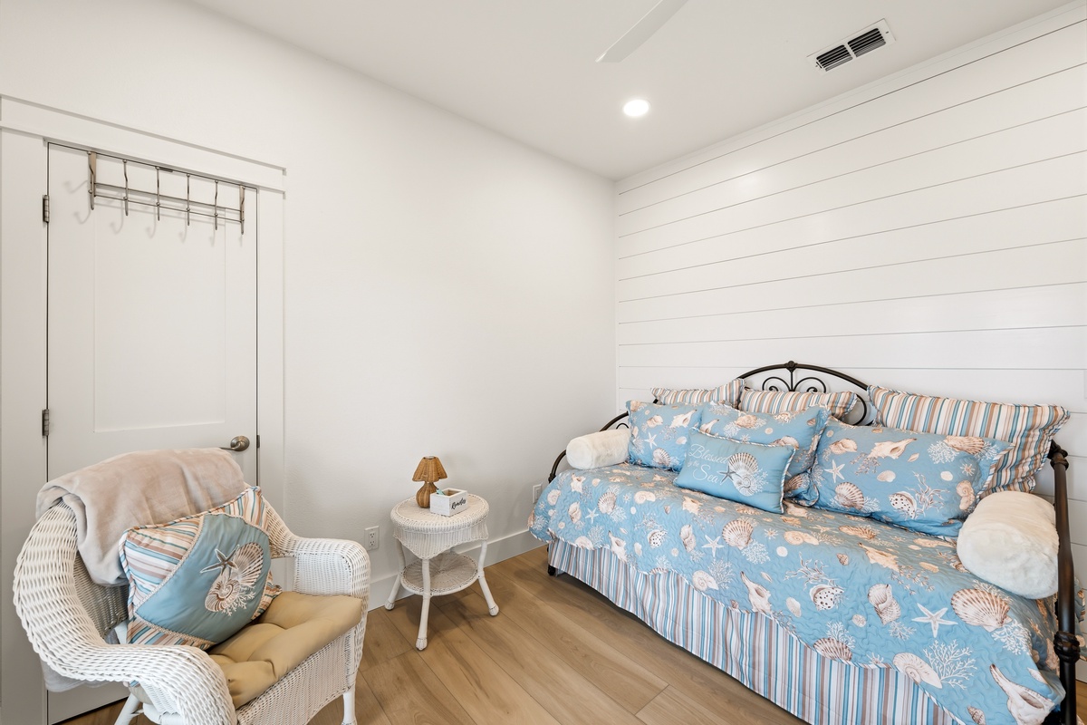 Slip into your cozy coastal retreat, where cheerful blue linens and beach-themed pillows invite peaceful sleep. A sunny wicker chair offers the perfect nook to start your morning coffee or curl up with a good book.