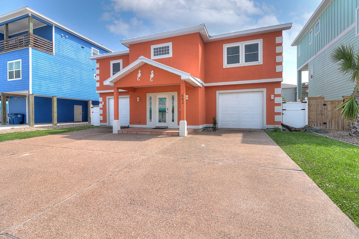 Bright coral beach house with covered entry and spacious driveway in a colorful coastal neighborhood.