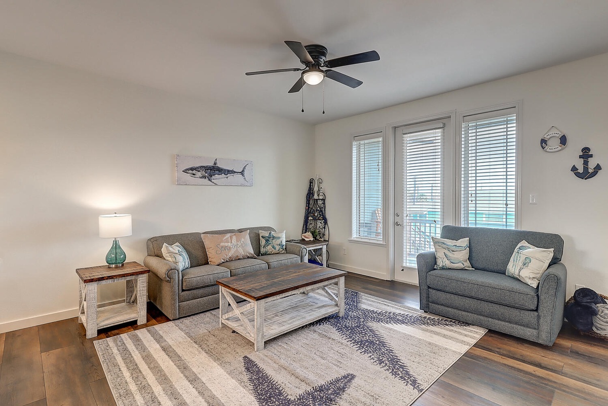 Relax in your coastal-themed living room with comfortable seating, nautical decor, and French doors opening to your private balcony.
