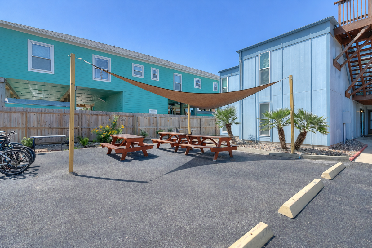 Modern property buildings with shaded outdoor seating area and tropical palm trees, creating a relaxed coastal atmosphere.