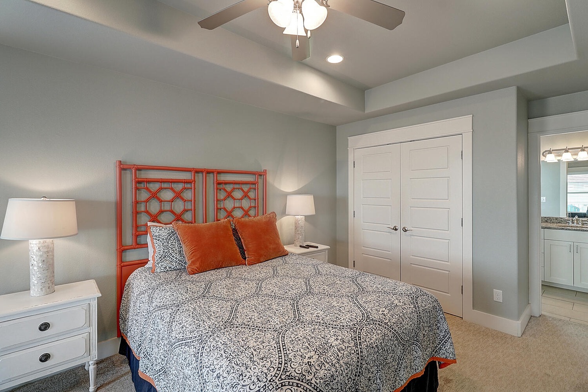 Your peaceful bedroom features a queen bed with vibrant coral headboard, soft linens, and gentle ceiling fan for comfort.