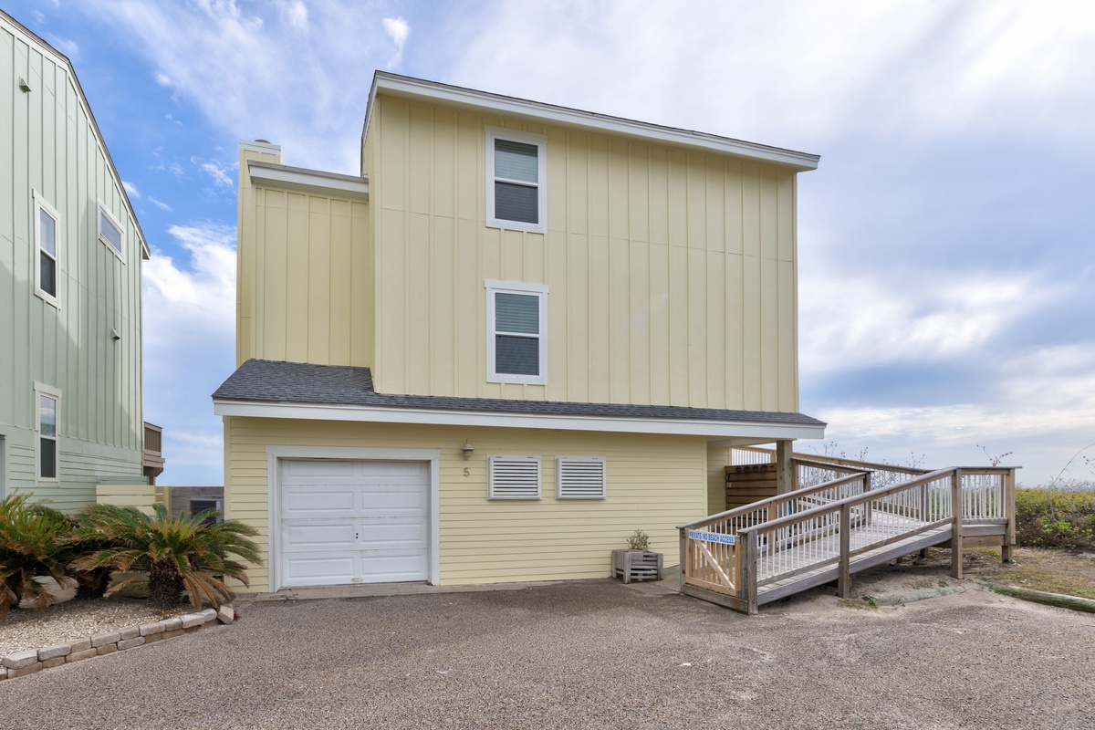 Charming beachside property with garage and elevated deck, nestled in a coastal neighborhood under bright blue skies.