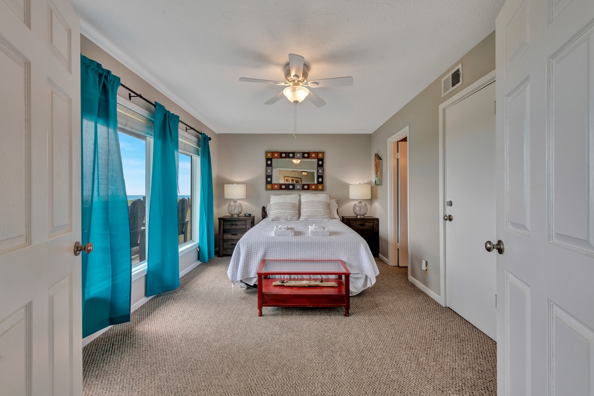 Relax in your spacious master bedroom featuring a plush king bed, vibrant turquoise curtains, and peaceful city views from your private window.
