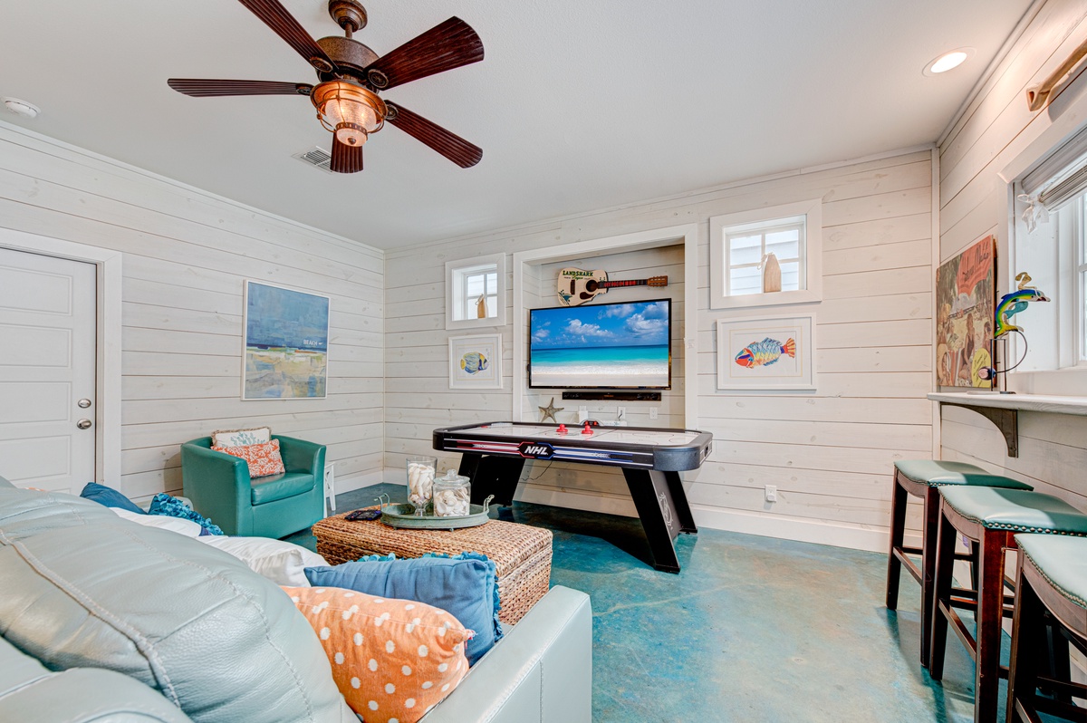 Unwind in your coastal game room with air hockey, plush seating, and beach-themed art creating the perfect family entertainment space.