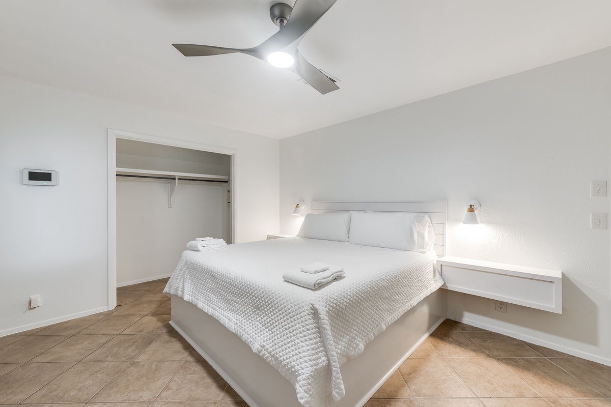 Drift off in this serene bedroom featuring crisp white linens, modern amenities, and thoughtful touches like reading lights for your comfort.