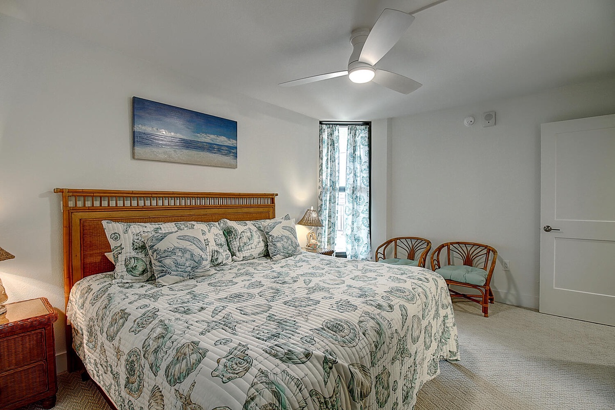 Relax in your peaceful bedroom sanctuary featuring a comfortable bed, coastal artwork, and gentle ceiling fan for perfect rest.