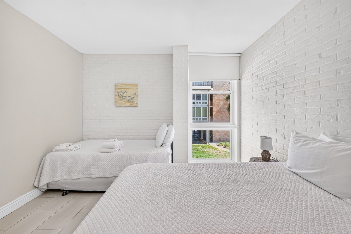 Drift off in this serene all-white bedroom where textured brick walls and plush bedding create your perfect retreat. Wake refreshed with natural light pouring through your window.