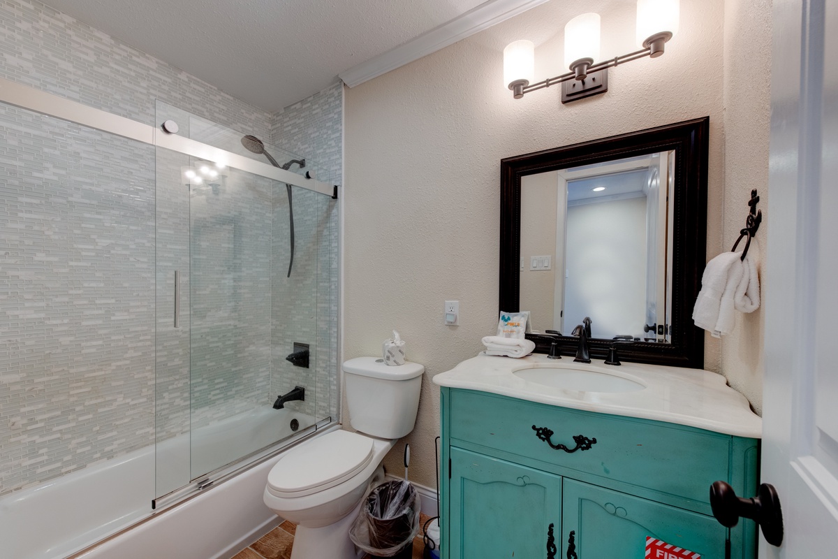 Step into your stylish bathroom featuring a refreshing teal vanity and spacious glass-enclosed shower for your daily refresh.