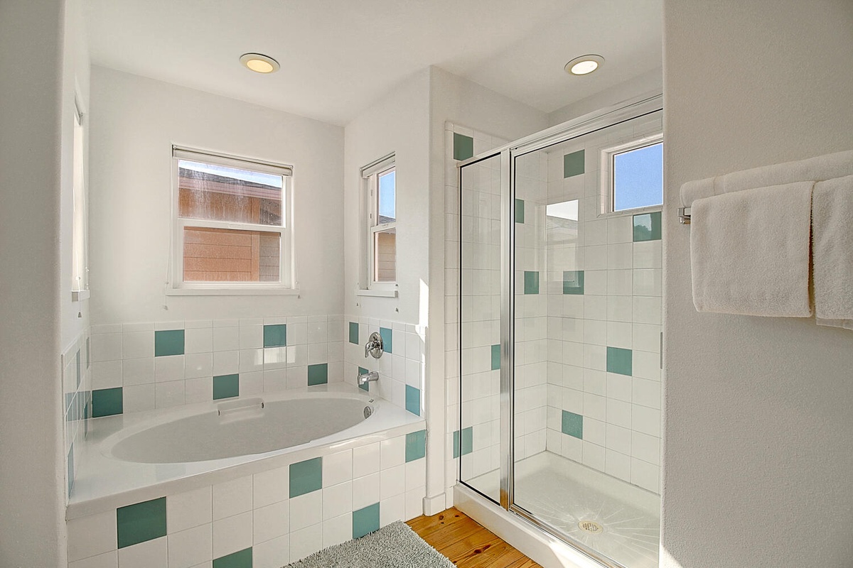 Unwind in your bright bathroom featuring a deep soaking tub and glass-enclosed shower with cheerful green accent tiles.