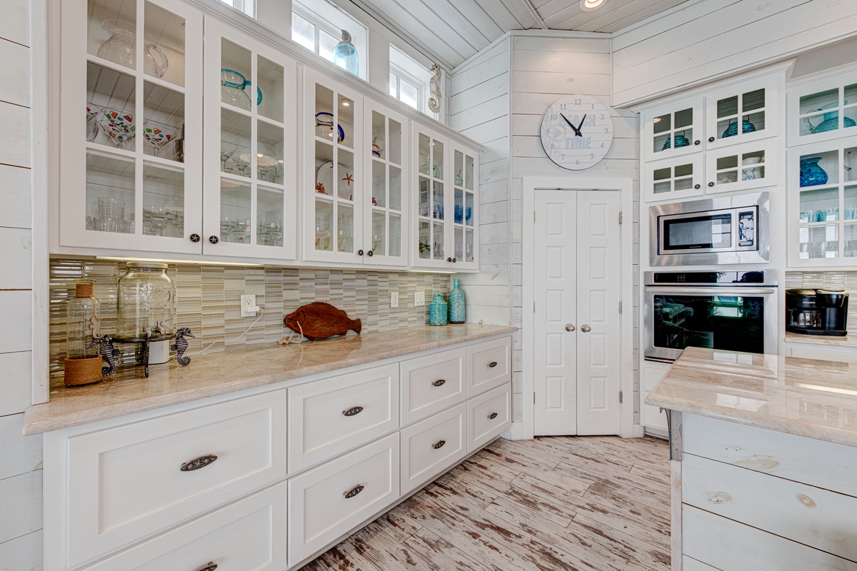 Your spacious coastal kitchen features gleaming white cabinetry, elegant glass-front displays, and modern appliances perfect for preparing memorable meals.