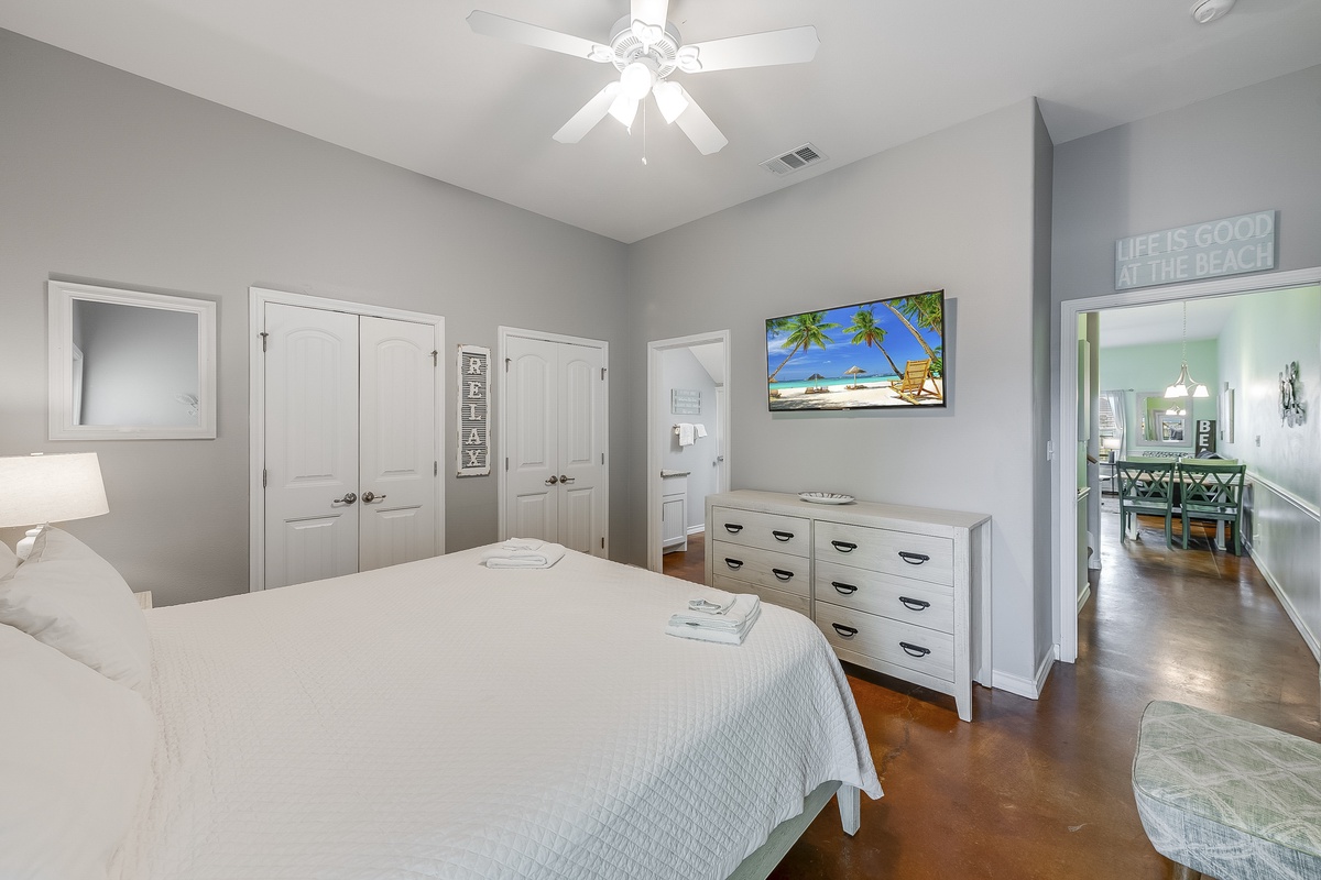 Unwind in your serene master bedroom featuring a ceiling fan, flat-screen TV, and coastal-themed decor that sets the perfect mood for relaxation.