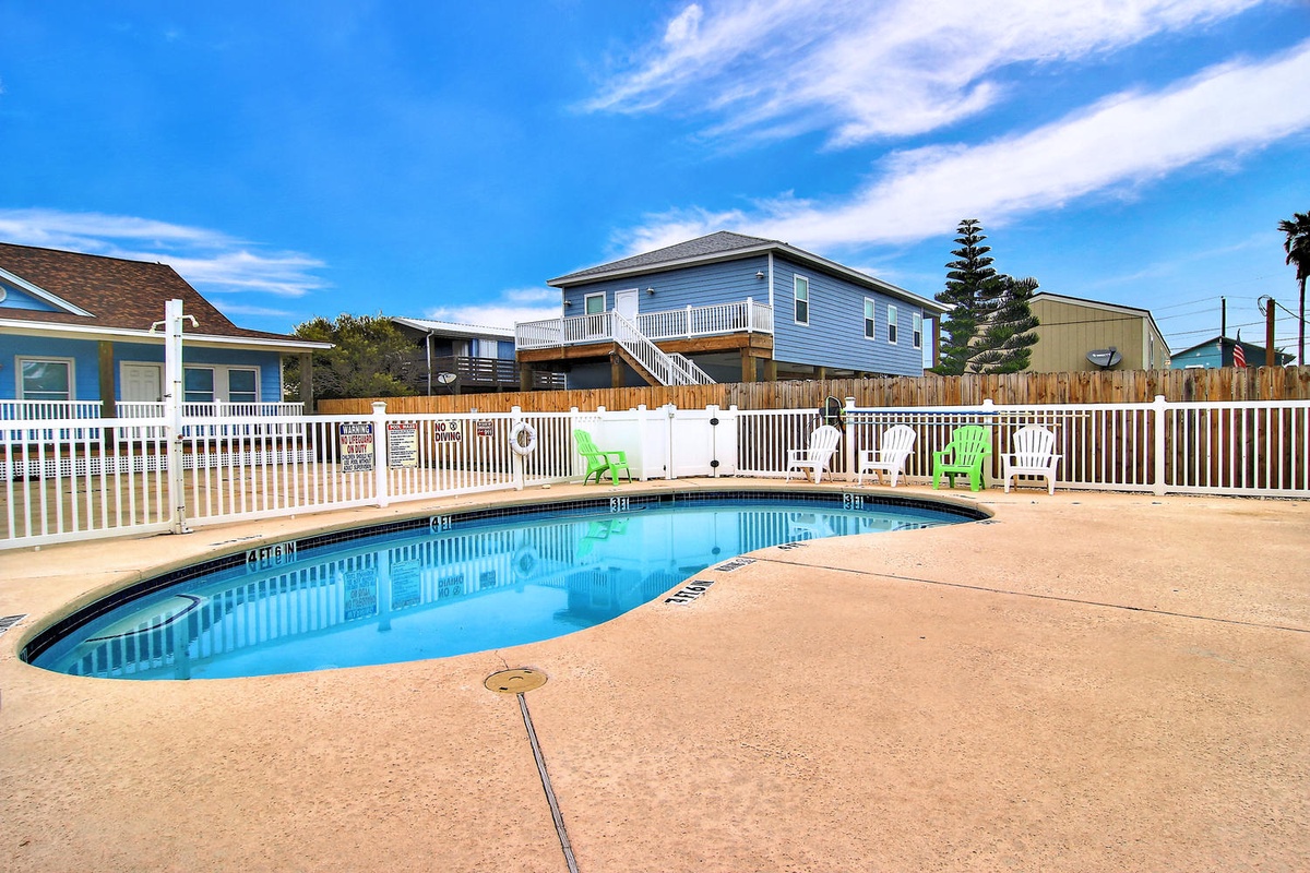 Sparkling pool area surrounded by coastal rental homes under brilliant blue skies.