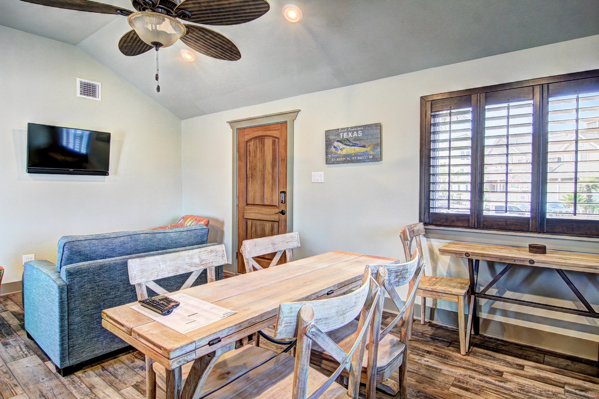 Your open-plan living space combines comfort and functionality with rustic wood dining table, cozy sofa, and modern TV for perfect relaxation.