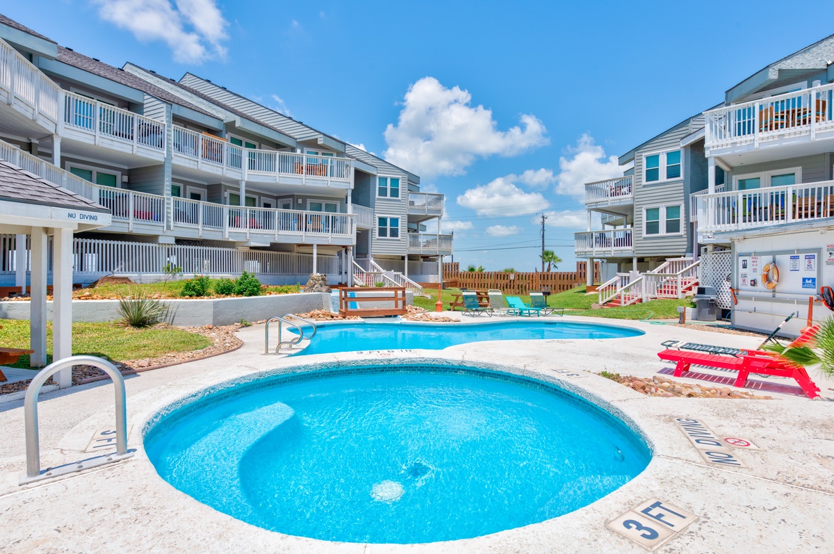 Crystal-clear pool complex with multiple levels for relaxation surrounded by colorful beach houses under bright blue skies.