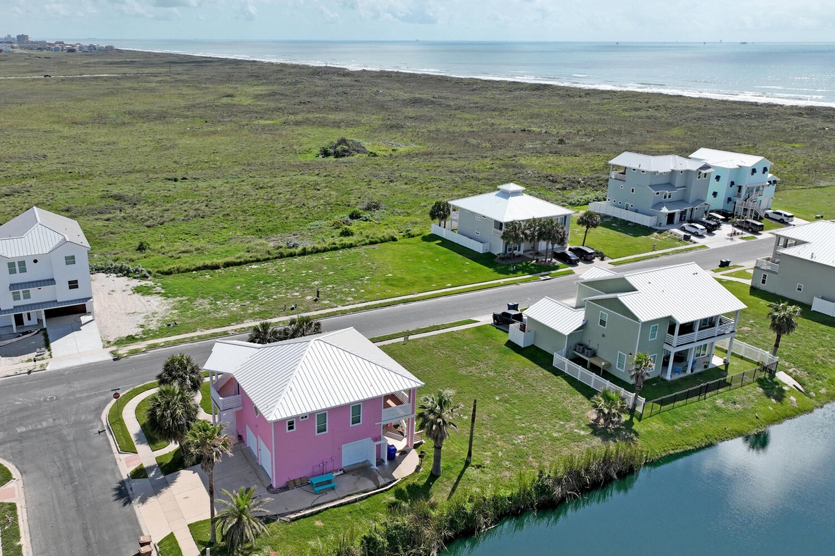 Aerial view of coastal vacation rental community featuring colorful homes between ocean and canal waterways.