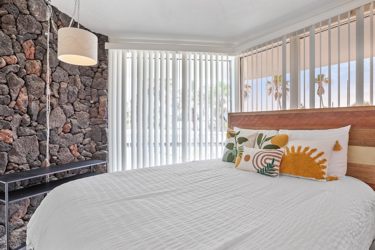 Rest in style with this comfortable bed and modern pendant lighting. Stone accent wall adds character while palm trees outside create a tropical feel.