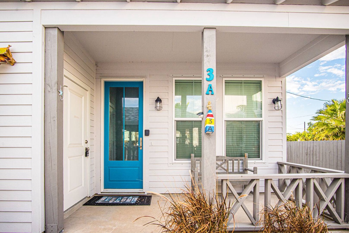 Cheerful beach house entrance with bright blue door and covered porch featuring outdoor seating area.