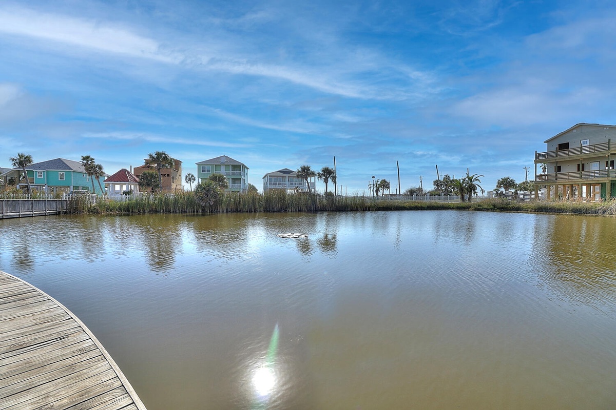 Peaceful waterfront community with colorful beach houses and palm trees surrounding a tranquil lagoon under bright blue skies.