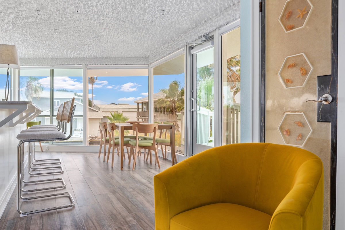 Your bright open-plan living space features a vibrant yellow accent chair and seamless indoor-outdoor flow through expansive glass doors to your private patio.