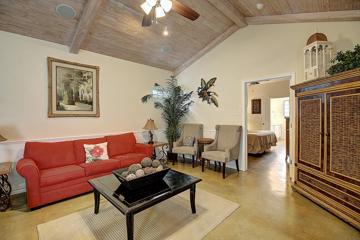 Relax in your elegant living space with soaring wood-beam ceilings, vibrant coral sofa, and tropical touches creating a warm, tropical retreat.