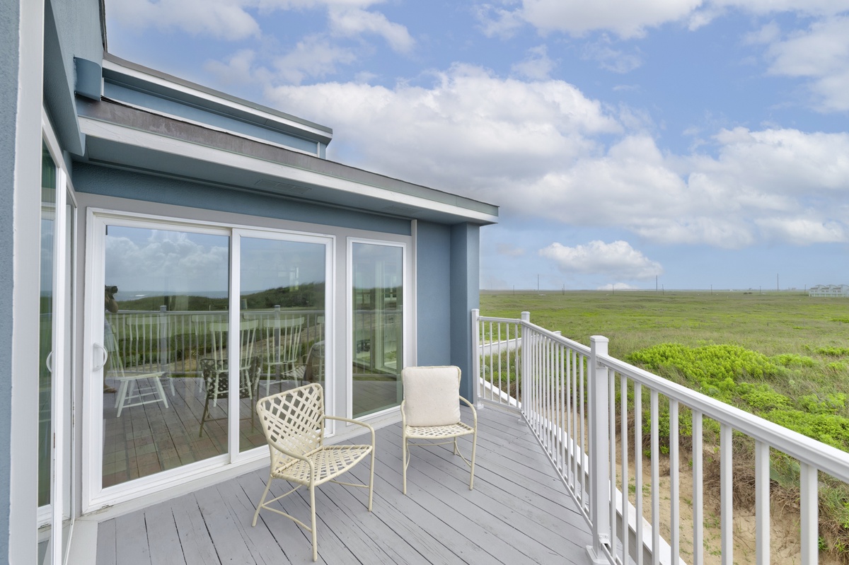 Modern coastal property featuring sleek architecture with expansive windows overlooking open countryside and distant wind turbines.