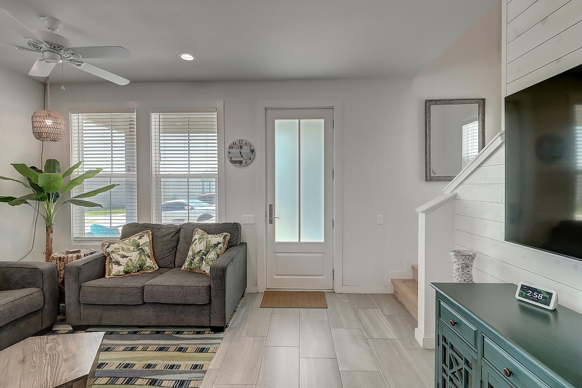 Relax in your bright, modern living room featuring comfortable gray seating, tropical accents, and a peaceful atmosphere perfect for unwinding.