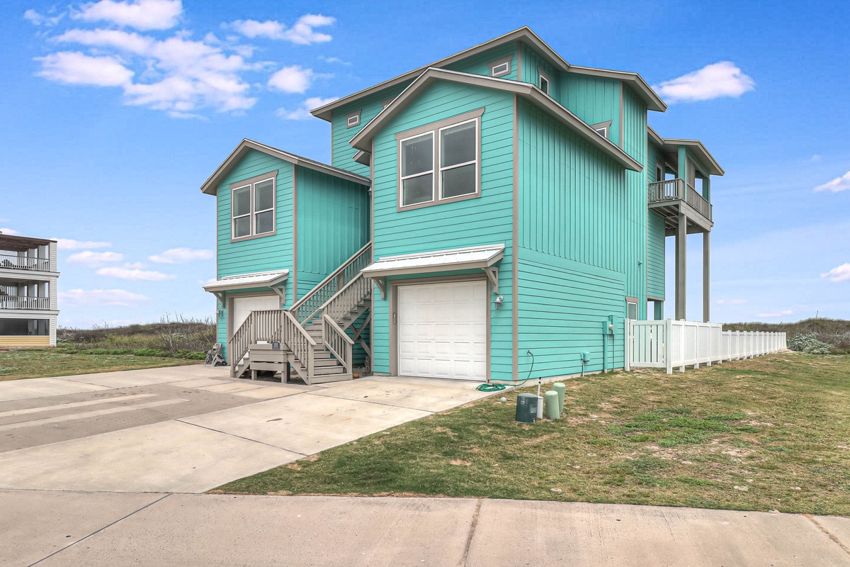 Charming turquoise beach house with elevated design and garage, perfectly positioned in coastal neighborhood setting.