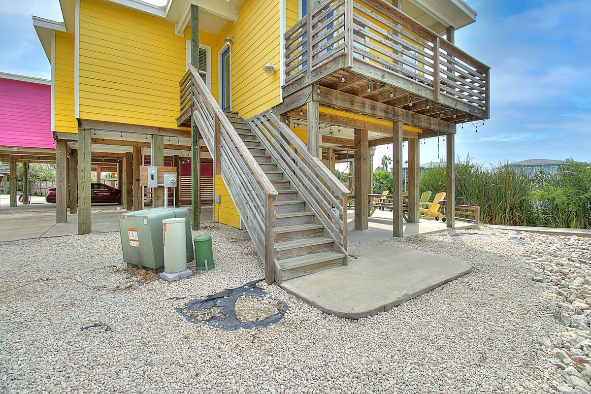 Colorful beachfront property featuring vibrant yellow and pink elevated homes with wooden staircases and covered parking areas.