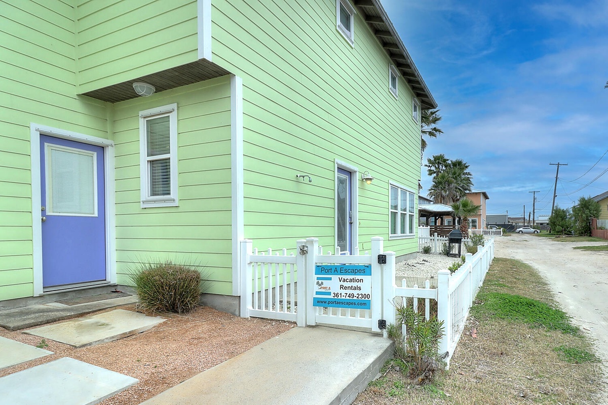 A bright green beach house with cheerful blue door welcomes guests to this coastal Port A Escapes vacation rental.