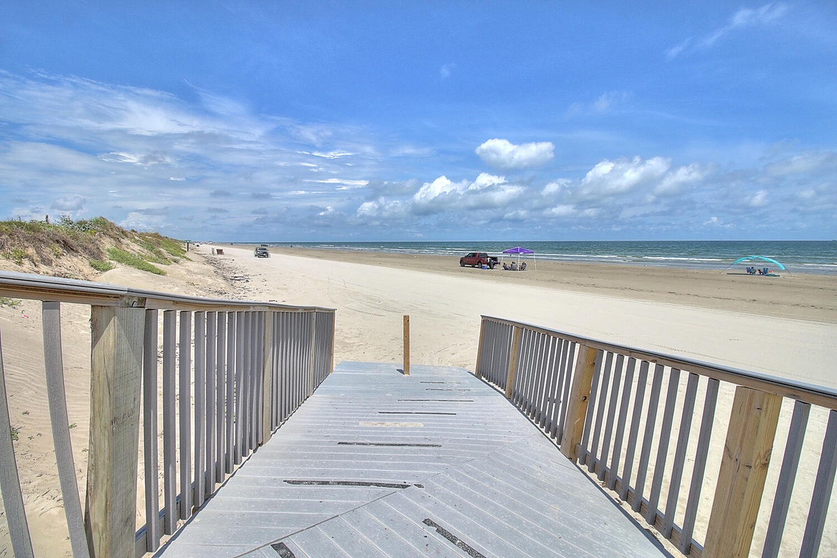 Wooden boardwalk leads directly to pristine sandy coastline with ocean views.