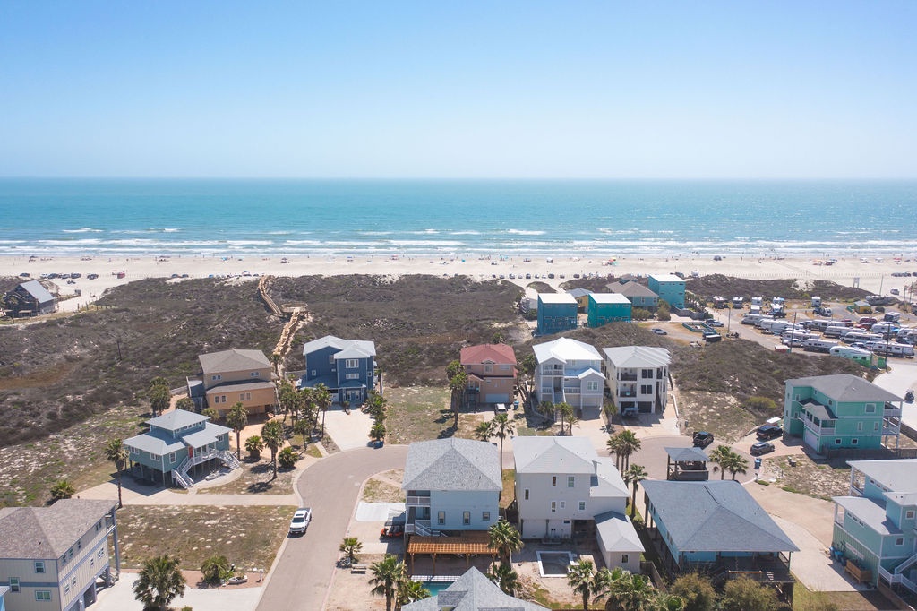 Aerial view of coastal vacation homes nestled between scenic beachfront and turquoise waters, perfect for a peaceful getaway.