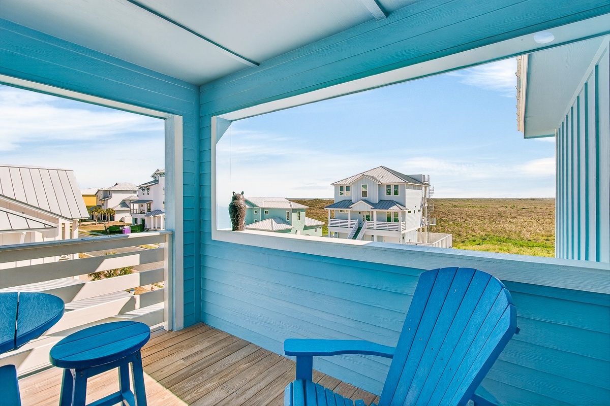 Relax on your private balcony with cheerful blue seating, gazing out at charming coastal homes and endless horizons.