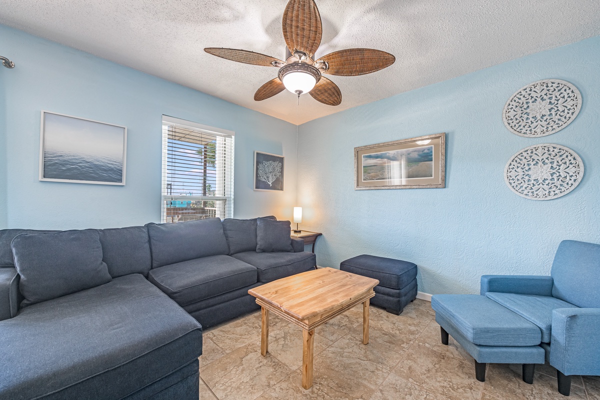 Unwind in your serene living space with coastal-inspired décor, plush seating, and a gentle ceiling fan creating the perfect atmosphere for relaxation.