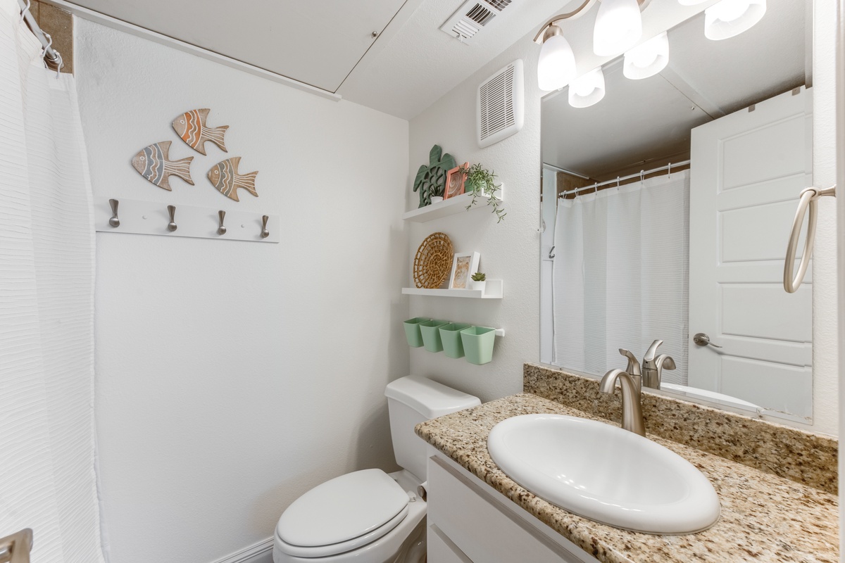 Your coastal-themed bathroom features granite countertops, thoughtful shelving, and charming fish wall art for a refreshing seaside retreat.