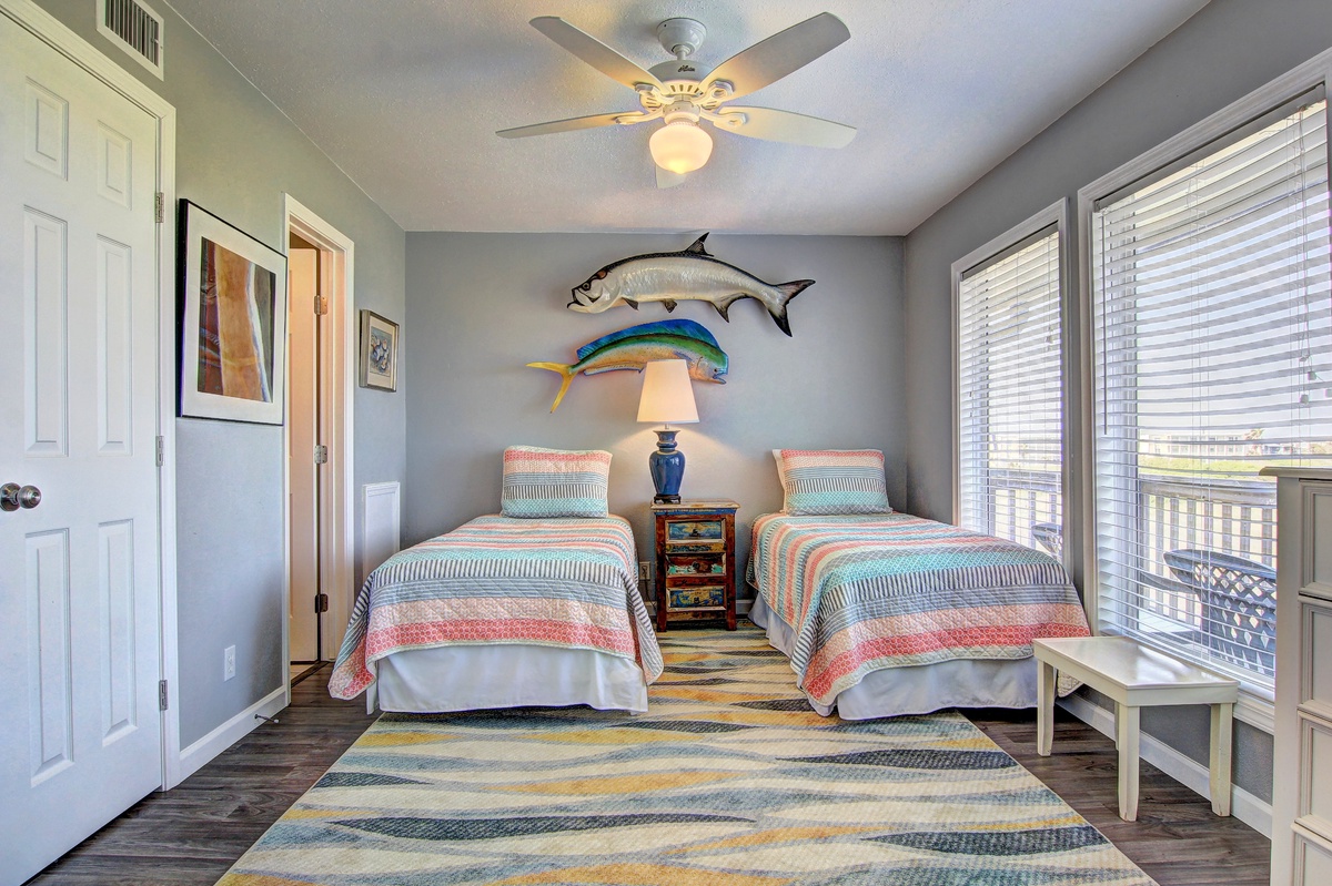 Drift off in this charming twin bedroom featuring coastal-themed decor, comfortable beds with colorful quilts, and large windows filling your space with natural light.
