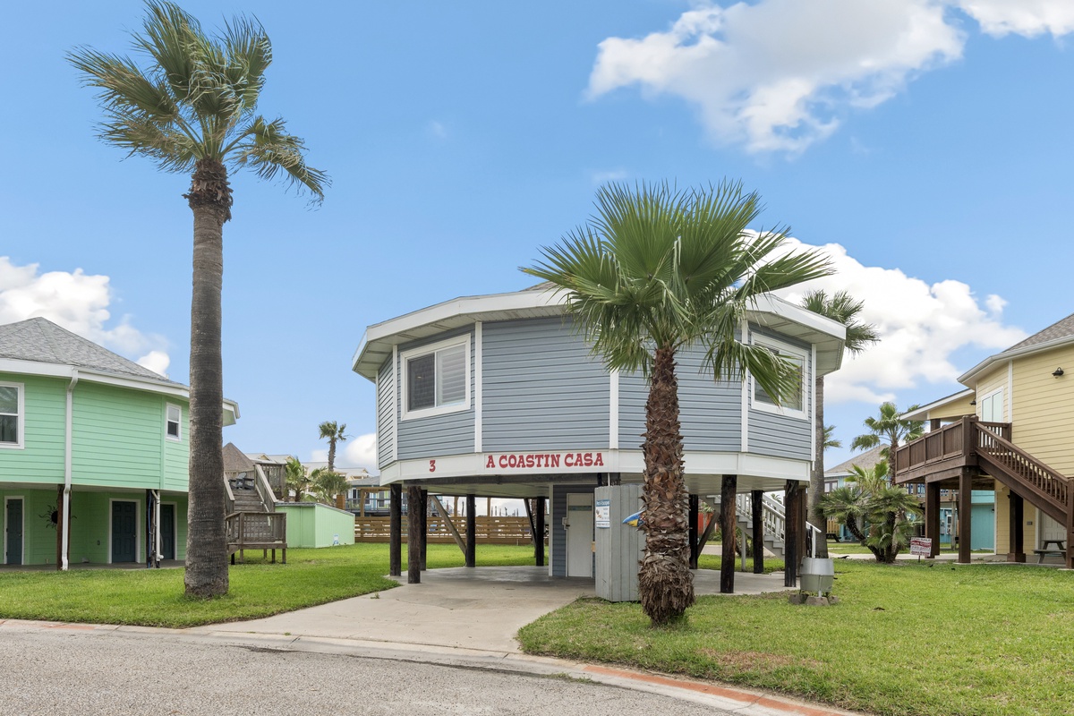 Coastal charm awaits at this elevated beach house, surrounded by swaying palms and colorful neighboring homes in a tropical paradise.