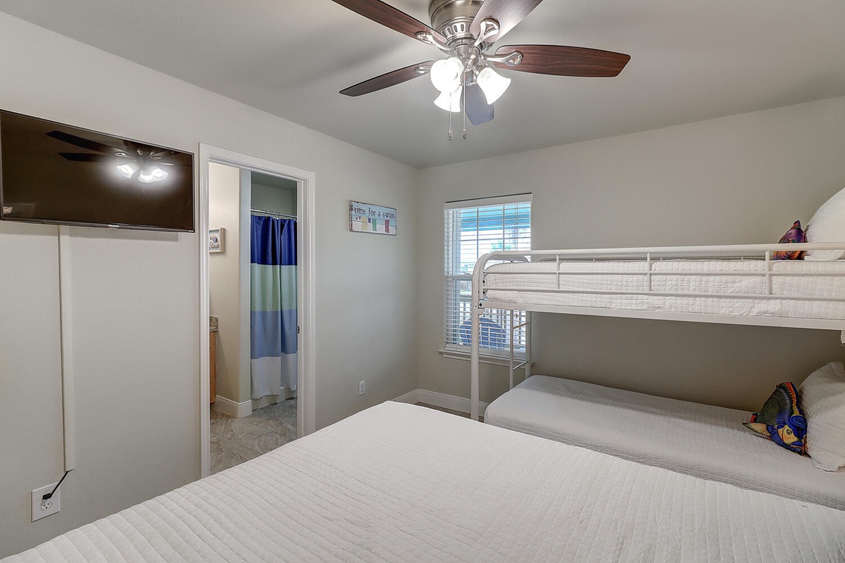 Your cozy bedroom features a comfortable queen bed and fun bunk beds, perfect for families. The ceiling fan keeps you cool while natural light brightens your coastal retreat.
