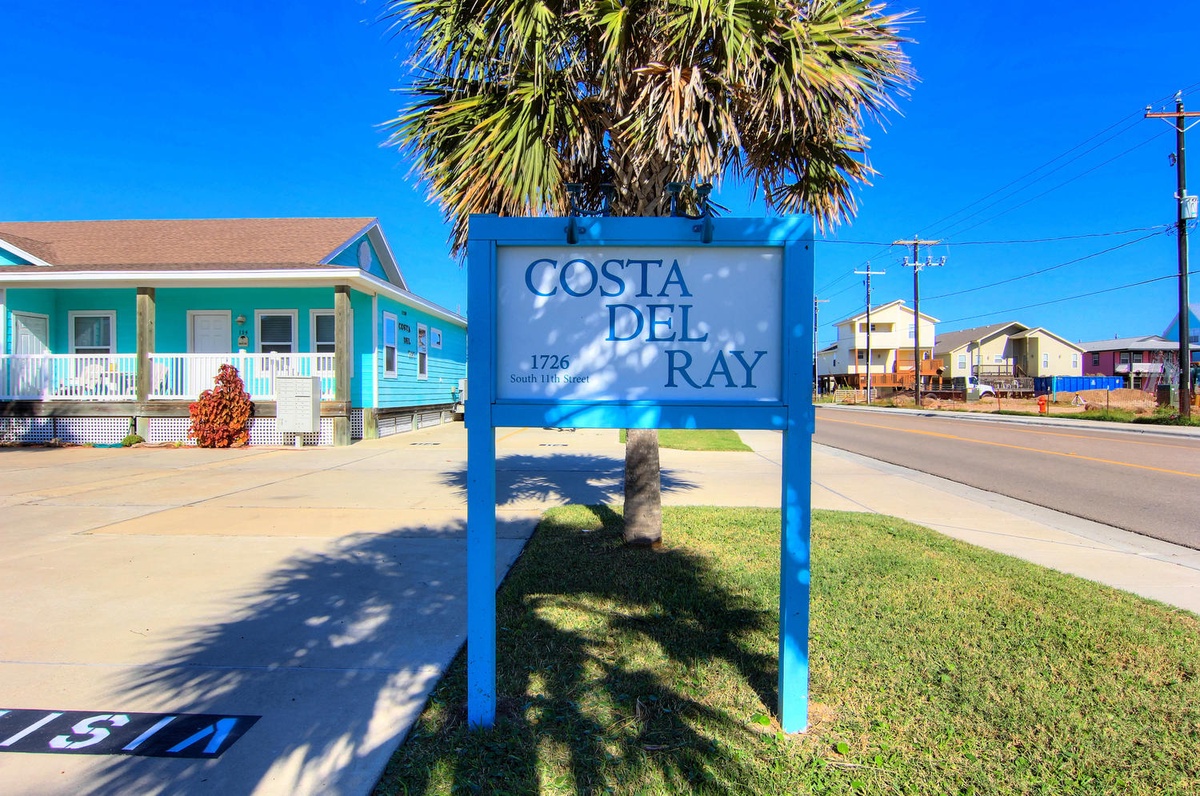 Costa Del Ray property entrance sign marking this charming coastal vacation rental destination with colorful beach houses nearby.