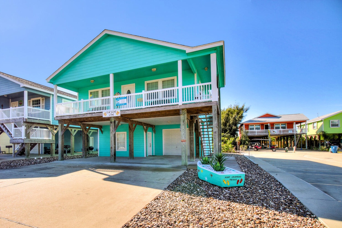 Vibrant coastal home with elevated design and covered parking beneath bright blue skies.