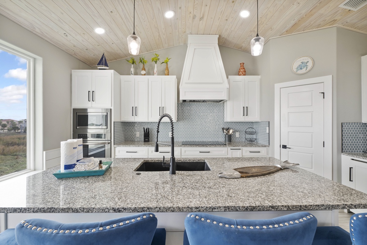 Your gourmet kitchen awaits with granite counters, modern appliances, and cozy breakfast bar seating beneath rustic wood ceilings.