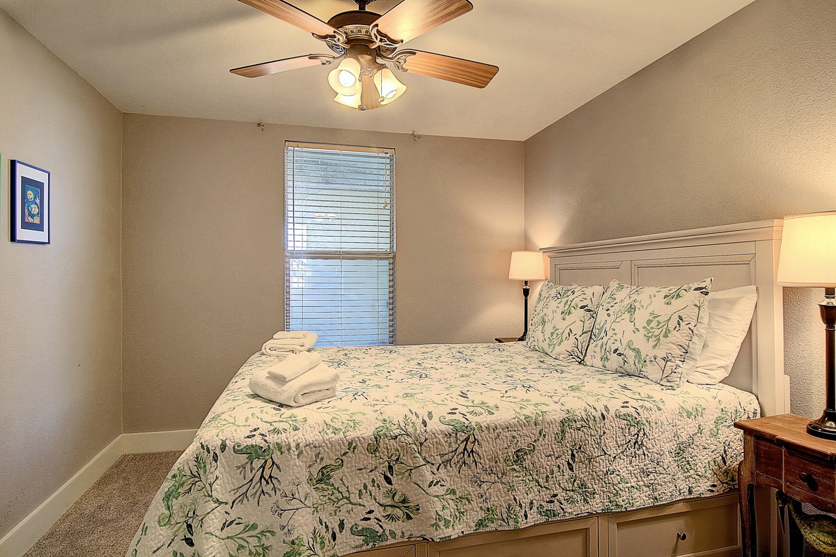 Your peaceful bedroom retreat features a comfortable queen bed, gentle ceiling fan, and warm bedside lighting for restful nights.
