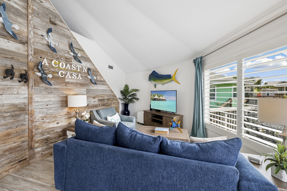 Relax in your coastal-themed living room with rustic wood walls, plush navy seating, and tropical touches creating the perfect beach house atmosphere.