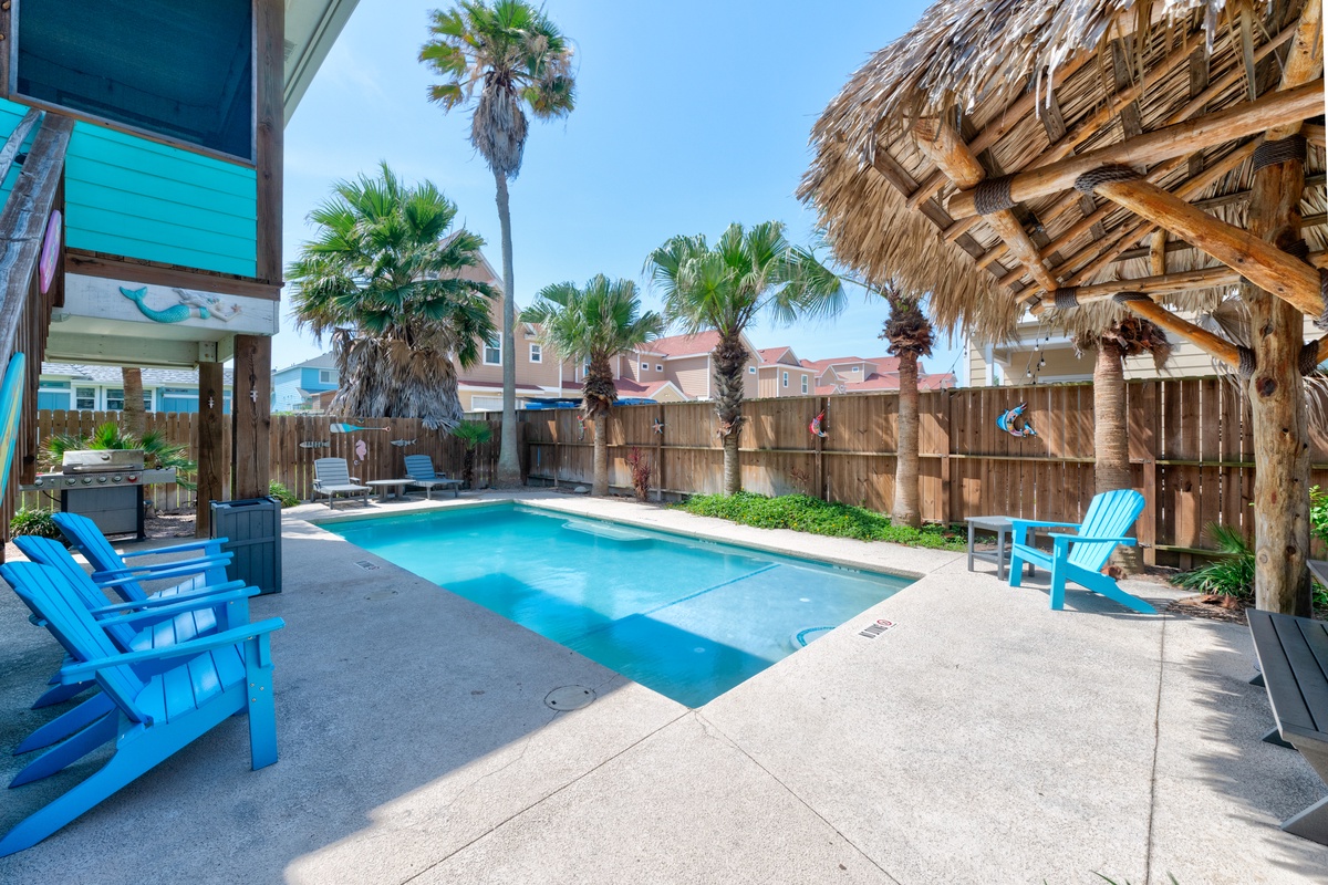 Your private oasis awaits with a sparkling pool, tropical palms, and vibrant blue loungers for ultimate relaxation under the sun.