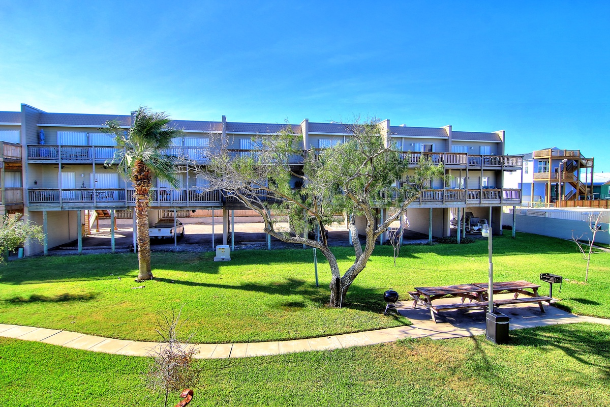 Multi-story beachfront property featuring spacious grounds with palm trees and outdoor recreational areas.