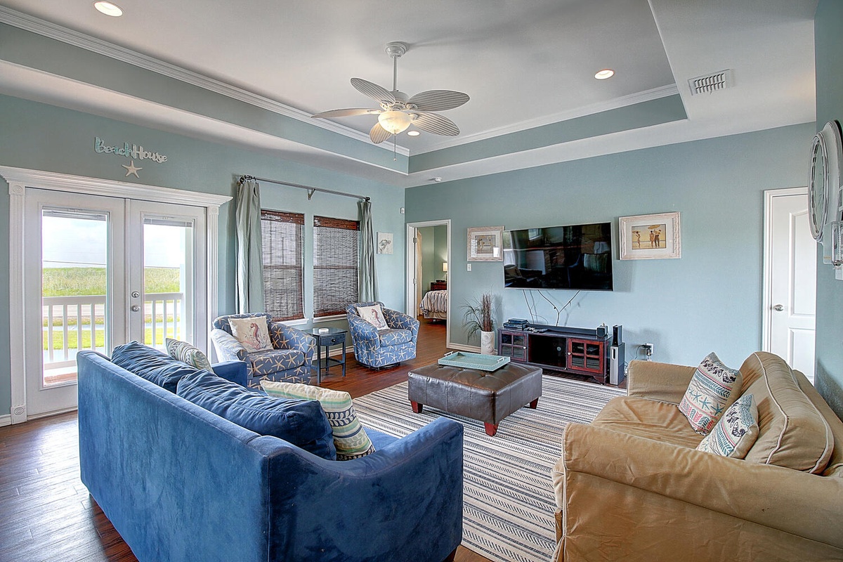 Unwind in your coastal living room featuring plush seating, entertainment center, and balcony doors opening to scenic views.
